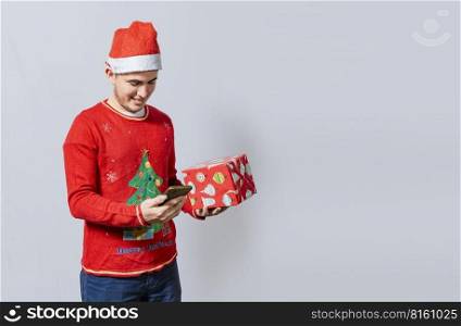 Christmas man holding gift box and telephone isolated. Handsome man in christmas hat holding gift and looking phone, Guy in christmas hat holding gift box and smiling at smartphone
