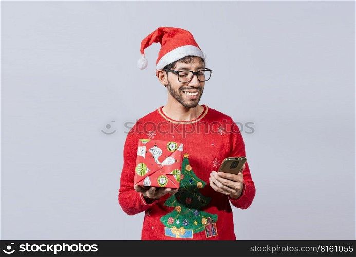 Christmas man holding gift box and telephone isolated. Handsome man in christmas hat holding gift and looking at phone, Guy in christmas hat holding gift box and smiling at smartphone