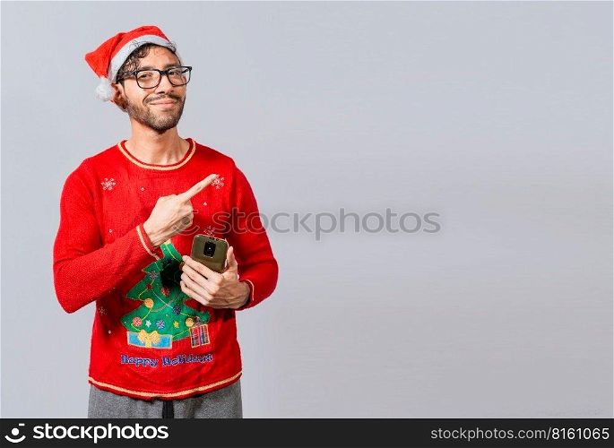 Christmas man holding phone pointing to the side. Smiling young man in christmas hat with cellphone pointing at promo. Christmas man concept with cell phone pointing to the side
