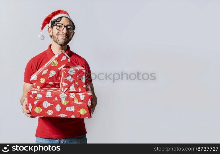 Christmas man portrait holding gift boxes and smiling isolated. Smiling guy in santa hat holding christmas gift boxes. Friendly man in christmas clothes holding gift boxes isolated