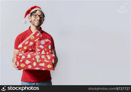 Christmas man portrait holding gift boxes and smiling isolated. Smiling guy in santa hat holding christmas gift boxes. Friendly man in christmas clothes holding gift boxes isolated