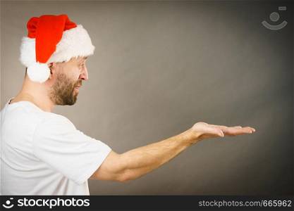 Christmas man wearing santa claus hat holding open hand palm with copy space for product text, side view on grey.. Christmas man with open hand copy space