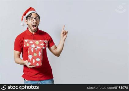 Christmas man with surprised face holding a gift pointing up. Amazed christmas man holding gifts pointing up. Surprised christmas man holding gifts and pointing up. Christmas man pointing a promo