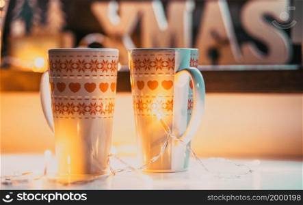 christmas mugs against holiday lights