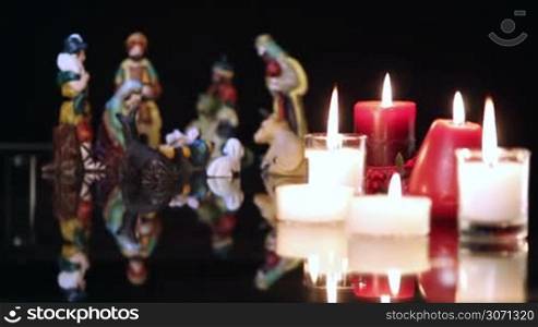 Christmas nativity scene with candles on black background. The focus moves from candles to figurines.