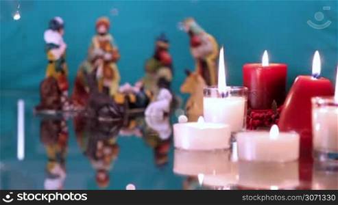 Christmas nativity scene with candles on green background with lights. The focus moves from candles to figurines.