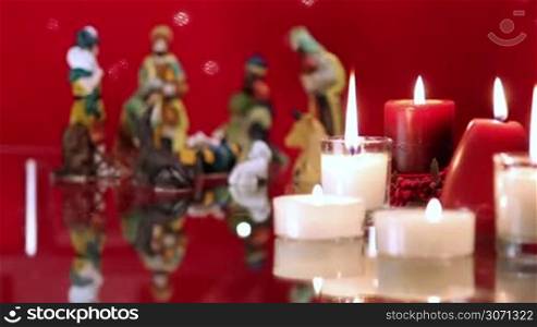 Christmas nativity scene with candles on red background with lights. The focus moves from candles to figurines.