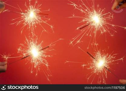 Christmas or Happy New Year party banner concept. Close up of Bright burning four sparklers on a red background.. Christmas or Happy New Year party banner concept. Close up of Bright burning four sparklers on a red