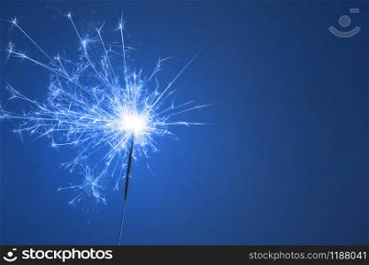 Christmas or Happy New Year party concept banner. Close up of Bright burning sparkler on a blue background. Copy space.. Christmas or Happy New Year party concept. Close up of Bright burning sparkler on a blue background.