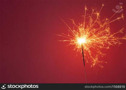 Christmas or Happy New Year party concept. Close up of Bright burning sparkler on a red background. Copy space.. Christmas or Happy New Year party concept. Close up of Bright burning sparkler on a red background.
