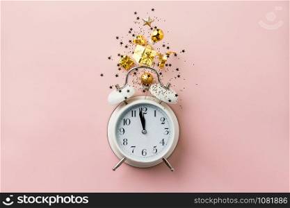 Christmas or New Year composition on pink background with retro alarm clock and Christmas decorations - stars, confetti, balls and gift boxes, top view, flat lay