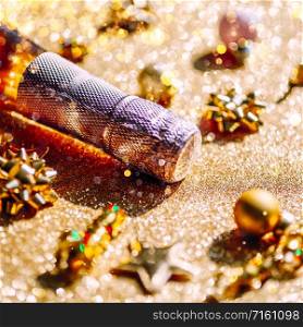 Christmas or New Year composition with bottle of rose champagne and golden sparkling decoration on golden shiny background, side view with festive bokeh and shadows. Party Celebration creative concept