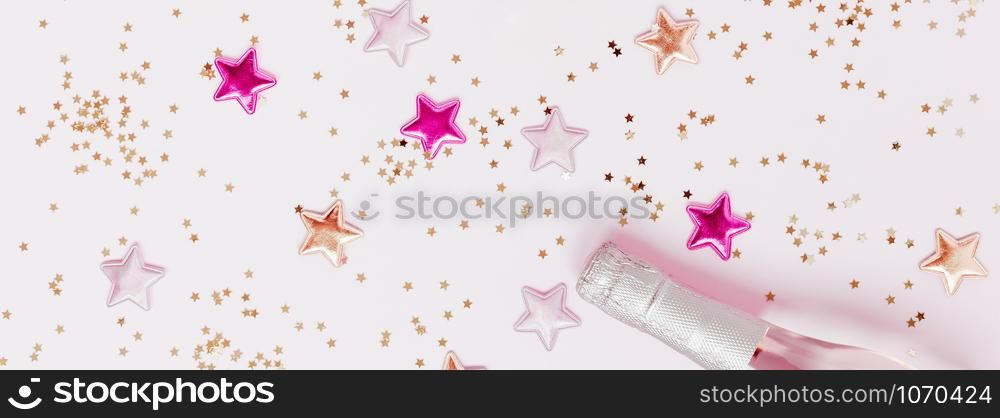 Christmas or New Year composition with bottles of rose champagne and golden shiny sparkle star confetti on pastel pink background, top view. Celebration flat lay. Party creative concept