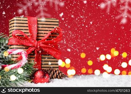 Christmas or New Year festive background. Gift box on red snowy Christmas or New Year festive background with blurred decorative lights