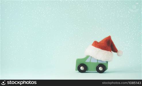 Christmas or New year minimal concept copy space background. The wooden toy car and Santa Claus hat on snow and mint color background.