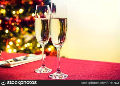 Christmas or New Year table decoration concept - champagne glasses and cutlery on a background of colorful Christmas tree decoration (vintage effect)