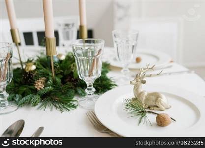 Christmas or new year table setting. Plates, silver Cutlery, glasses, gift box, festive branch decoration, candles, shiny deer on a white table background, selective focus