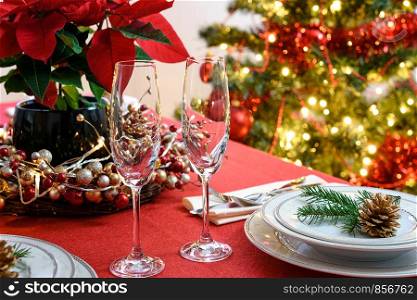 Christmas or New Years table decoration concept - champagne glasses, red poinsettia and table setting on a background of colorful Christmas decoration.