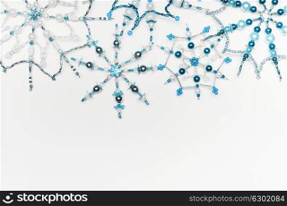 Christmas or winter concept. Border of various handmade blue snowflakes made from beads and bugle on white desk background, top view. Layout for greeting card and winter holidays