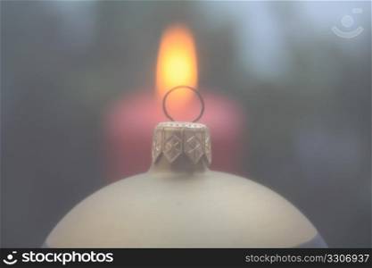 Christmas ornament in soft focus, burning candle in the background