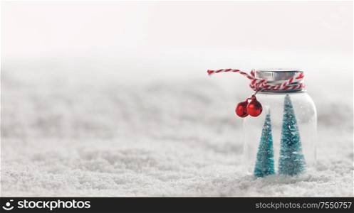 Christmas ornaments of glass jar with striped ribbon , bells and fir trees inside on snow background. Christmas ornaments on snow