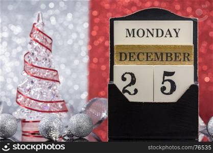 Christmas ornaments with wooden calendar and Christmas tree reflection on glass table over red an silver background