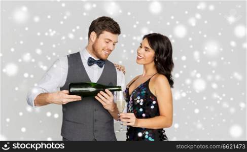christmas party, new year celebration and holidays concept - happy couple with bottle of non alcoholic champagne and wine glasses over grey background and snow. happy couple with champagne celebrating christmas