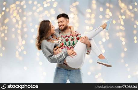 christmas, people and holidays concept - happy couple at ugly sweater party over festive lights background. happy couple at christmas ugly sweater party