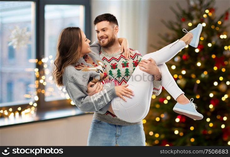 christmas, people and holidays concept - happy couple at ugly sweater party over home room background. happy couple at christmas ugly sweater party