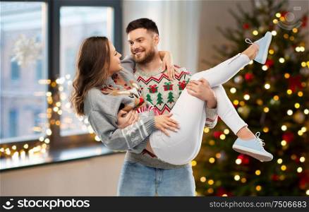christmas, people and holidays concept - happy couple at ugly sweater party over home room background. happy couple at christmas ugly sweater party