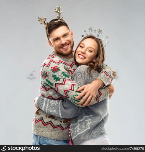 christmas, people and holidays concept - happy couple hugging at ugly sweater party. happy couple at christmas ugly sweater party