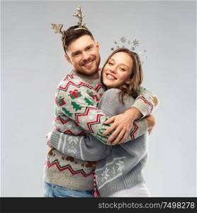christmas, people and holidays concept - happy couple hugging at ugly sweater party. happy couple at christmas ugly sweater party