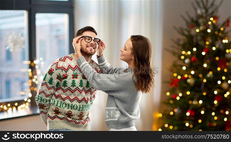 christmas, people and holidays concept - happy couple in ugly sweaters over home background. happy couple in ugly sweaters at home on christmas