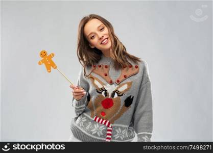 christmas, people and holidays concept - happy young woman in jumper with reindeer pattern holding gingerbread accessory at ugly sweater party. woman in christmas sweater with reindeer pattern