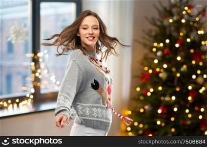 christmas, people and holidays concept - happy young woman in jumper with reindeer pattern dancing at ugly sweater party over home room background. woman dancing at christmas ugly sweater party