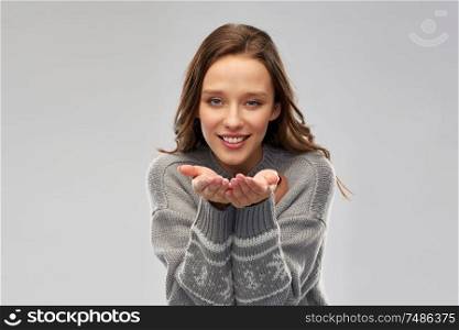christmas, people and holidays concept - happy young woman wearing ugly sweater with reindeer pattern holding something imaginary over grey background. woman in ugly christmas sweater holding something