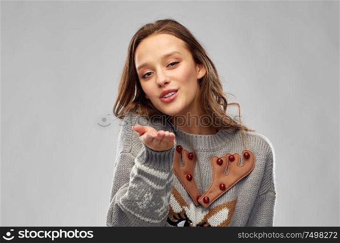 christmas, people and holidays concept - happy young woman wearing ugly sweater with reindeer pattern sending air kiss over grey background. woman in ugly christmas sweater sending air kiss