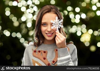 christmas, people and holidays concept - happy young woman with snowflake decoration wearing ugly sweater over festive lights on dark green background. woman in christmas sweater with reindeer pattern