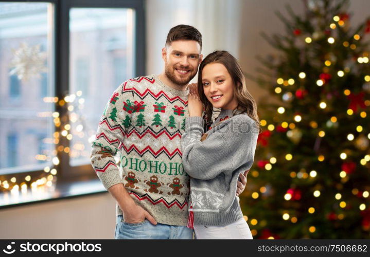 christmas, people and holidays concept - portrait of happy couple at ugly sweater party over home room background. happy couple at christmas ugly sweater party
