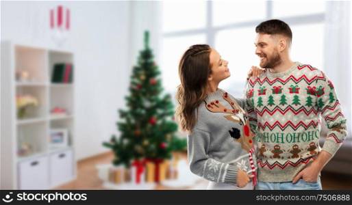 christmas, people and holidays concept - portrait of happy couple at ugly sweater party over home room background. happy couple at christmas ugly sweater party