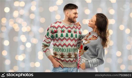 christmas, people and holidays concept - portrait of happy couple at ugly sweater party over festive lights background. happy couple at christmas ugly sweater party