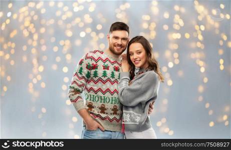 christmas, people and holidays concept - portrait of happy couple at ugly sweater party over festive lights background. happy couple at christmas ugly sweater party