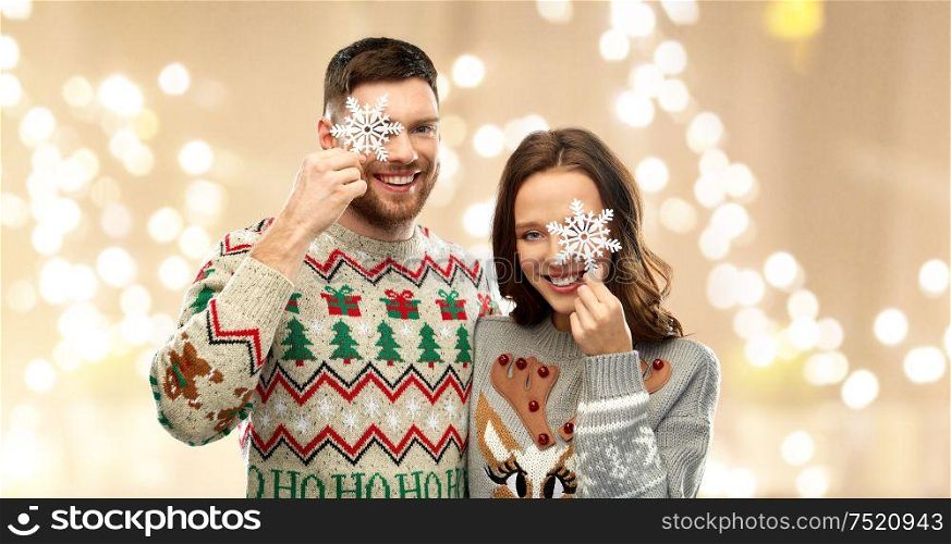 christmas, people and holidays concept - portrait of happy couple at ugly sweater party with snowflakes over festive lights background. happy couple at christmas ugly sweater party