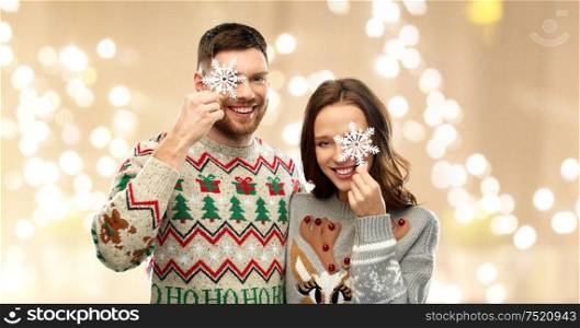 christmas, people and holidays concept - portrait of happy couple at ugly sweater party with snowflakes over festive lights background. happy couple at christmas ugly sweater party