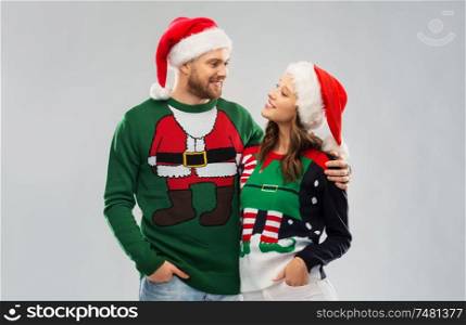 christmas, people and holidays concept - portrait of happy couple in santa hats at ugly sweater party. happy couple in christmas sweaters and santa hats