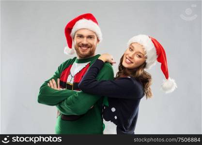 christmas, people and holidays concept - portrait of happy couple in santa hats at ugly sweater party. happy couple in christmas sweaters and santa hats