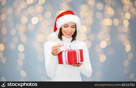 christmas, people and holidays concept - smiling woman in santa helper hat with gift box over lights background