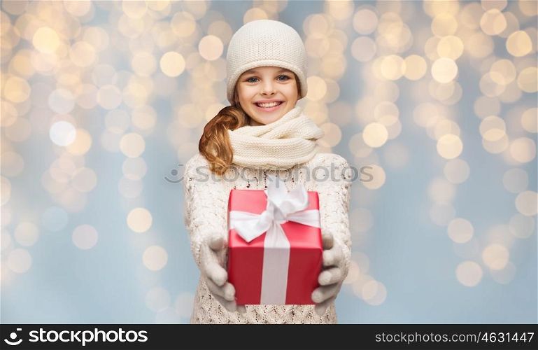 christmas, people, children and holidays concept - smiling girl in winter clothes with gift box over lights background