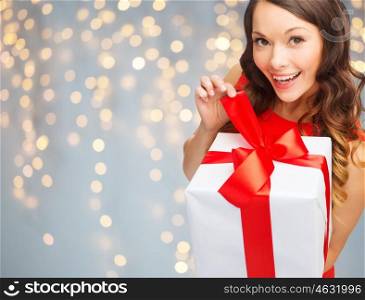 christmas, people, holidays and celebration concept - smiling woman in red dress with gift box over lights background