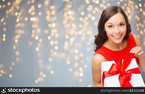 christmas, people, holidays and celebration concept - smiling woman in red dress with gift box over lights background. smiling woman in red dress with gift box